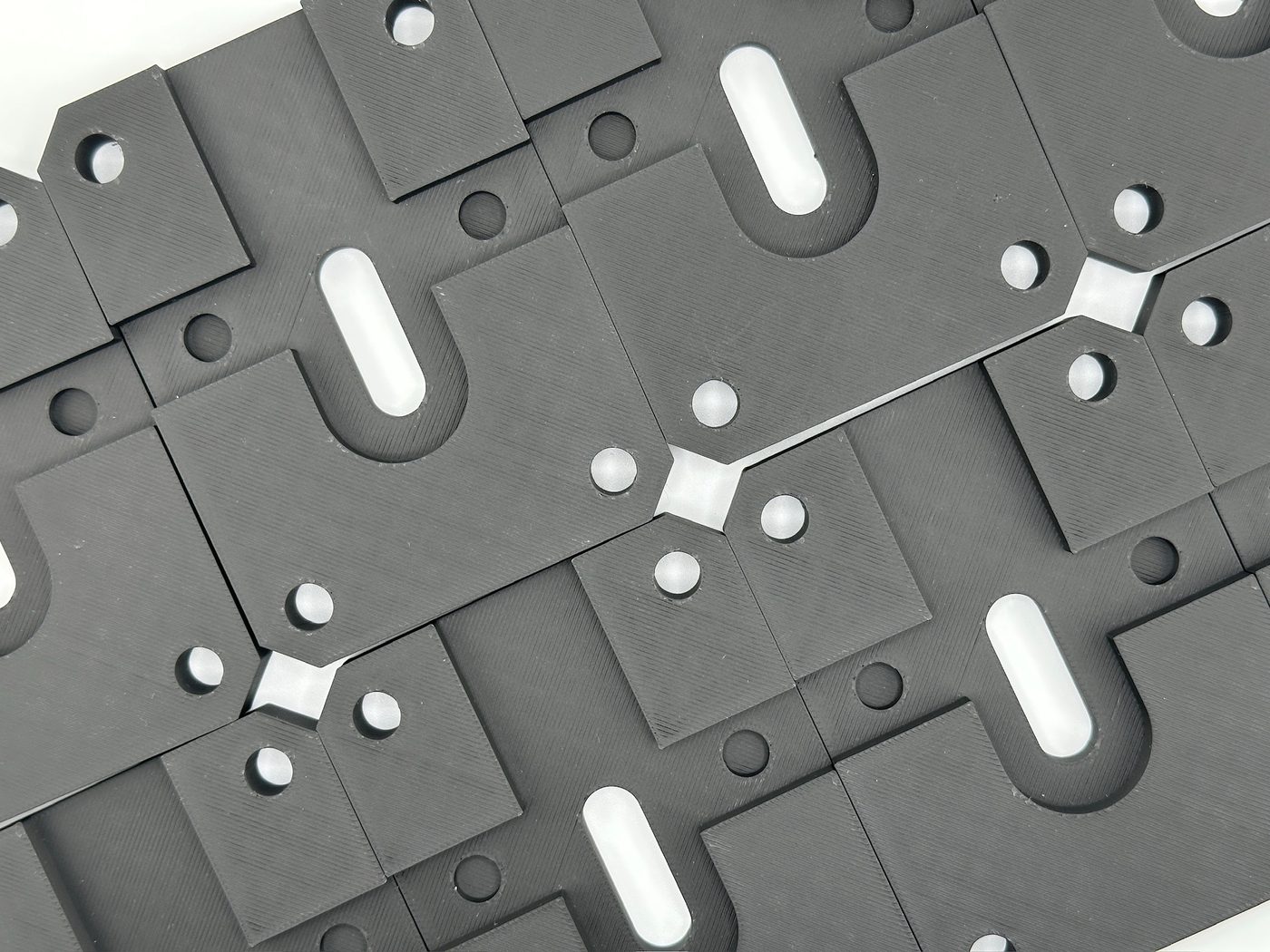 Batch of black FDM 3D printed fixture plates with precision slots and mounting holes