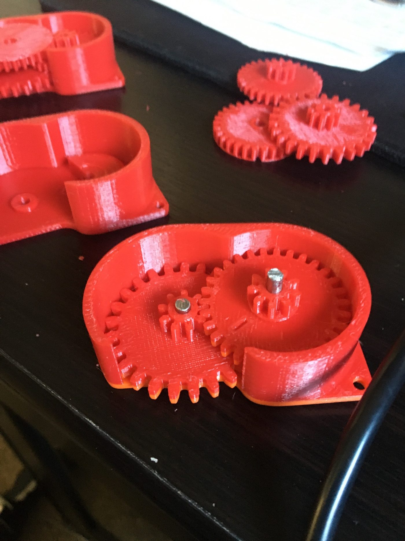 Red FDM 3D printed gearbox prototype with meshing spur gears and metal shafts showing functional design validation