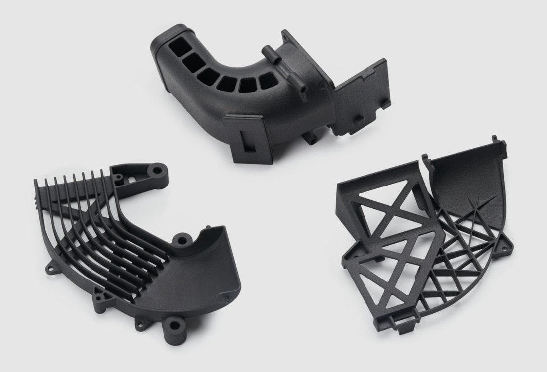 Three black-dyed MJF nylon parts: an intake duct, a finned bracket, and a lattice bracket