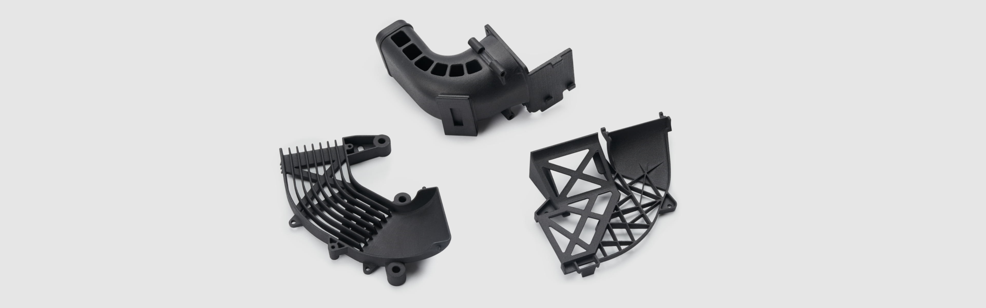 Three black MJF-printed nylon parts: an intake duct, a lattice bracket, and a structural frame showing complex geometry