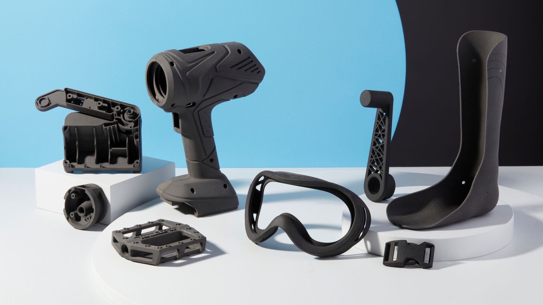 Collection of SLS 3D printed nylon parts including drill housing, goggles, prosthetic, pedal, and buckle
